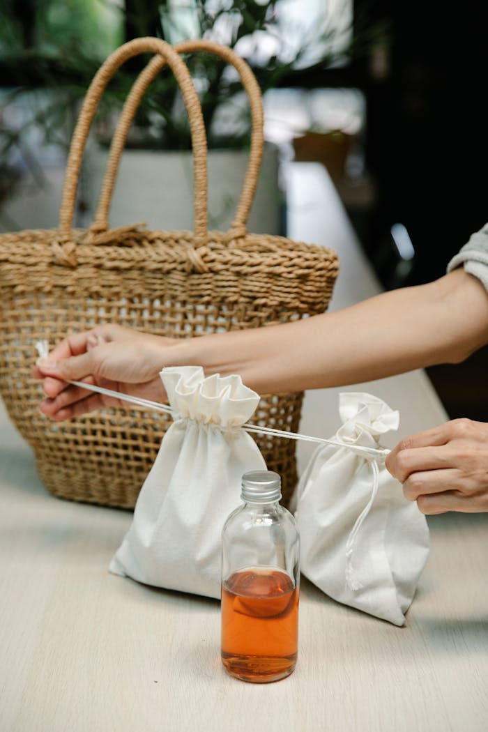 Person tying eco-friendly reusable bags with a glass bottle on a table.